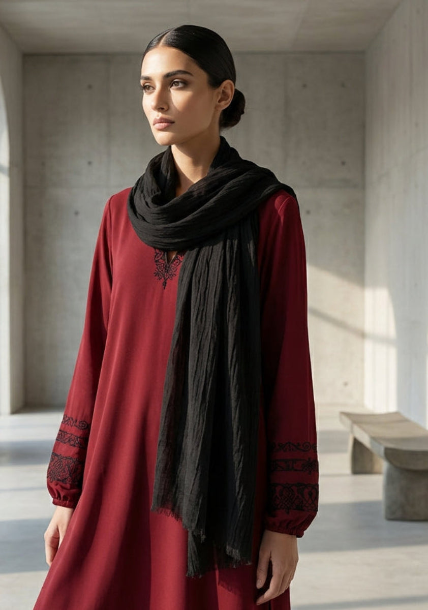 Woman in a red dress with a black scarf standing in a modern, sunlit room.