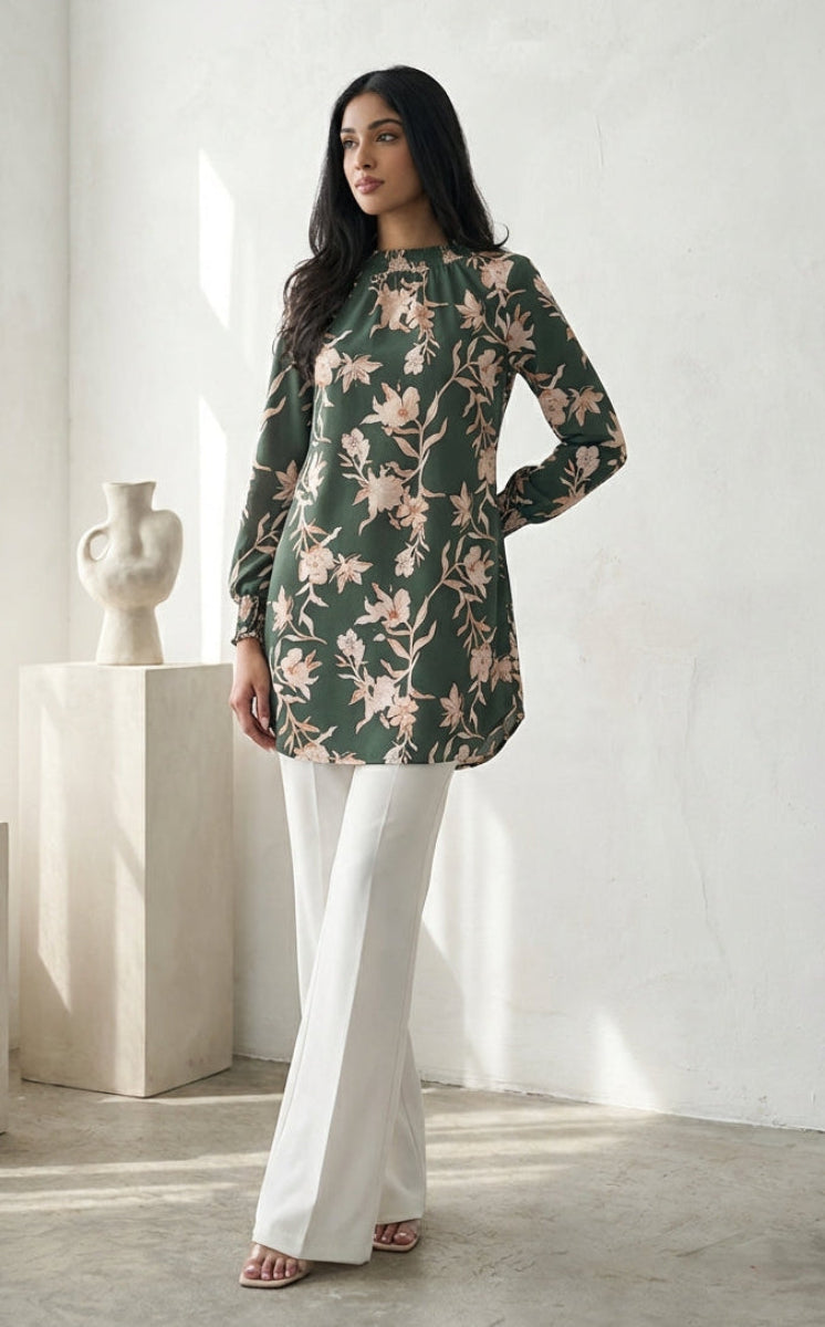 Woman wearing a floral dress and white pants in a minimalistic room with light-colored walls and flooring.