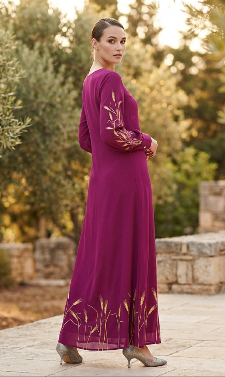 Woman in a long purple dress with floral embroidery standing in a scenic outdoor setting.