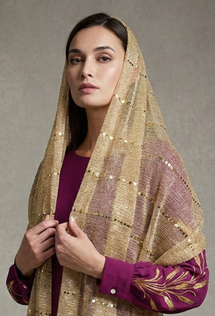 Woman wearing a purple dress with gold embroidery and a matching gold dupatta against a gray background