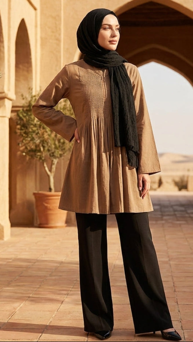 Woman in beige dress and black hijab standing in a desert setting with arches and potted plants.