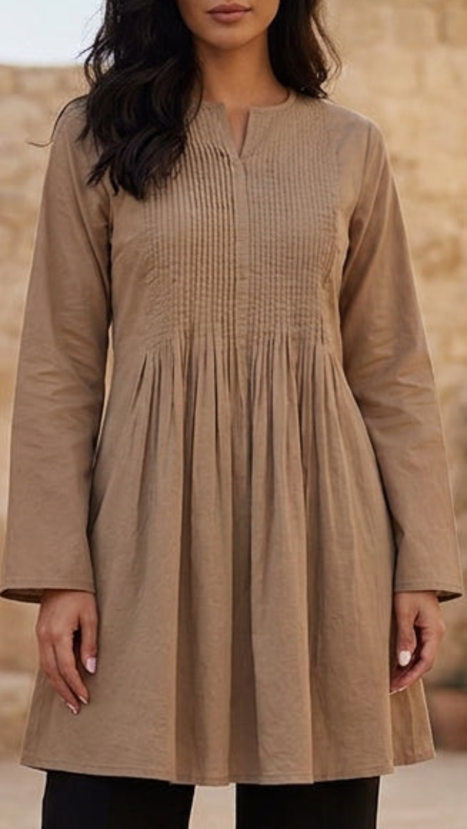 Woman in a beige dress standing in a sunlit stone courtyard with plants.