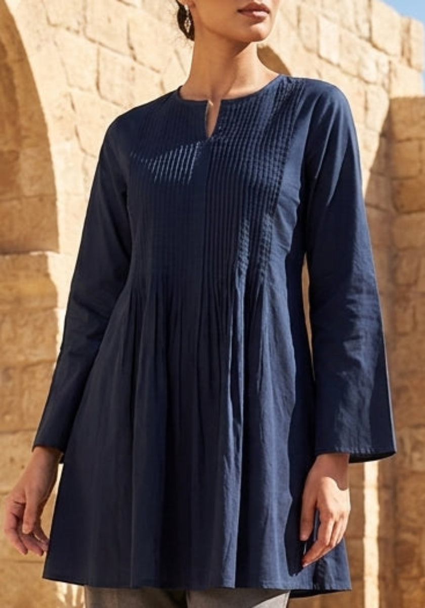 Woman in a blue dress standing in front of stone arches and desert landscape