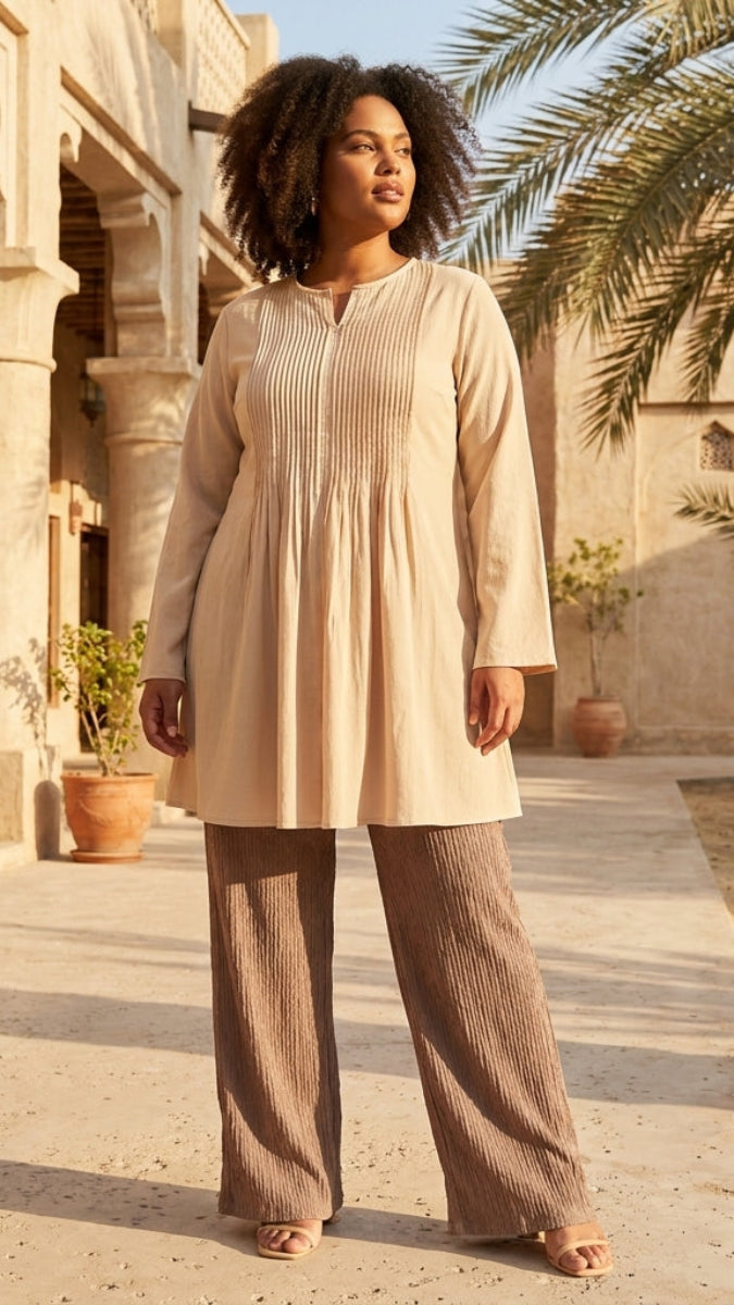 Woman in beige outfit standing in a sunlit courtyard with palm trees and architectural columns.