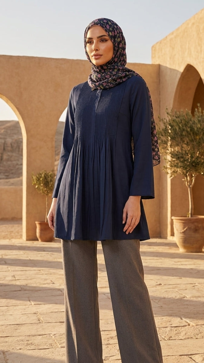 Woman in a blue dress and patterned hijab standing in a sunlit outdoor setting with arches and plants.