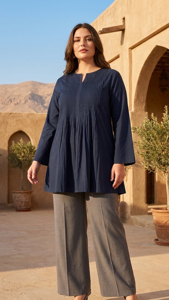 Woman wearing a navy blue top and gray pants standing in front of a desert-style building with arches and mountains.
