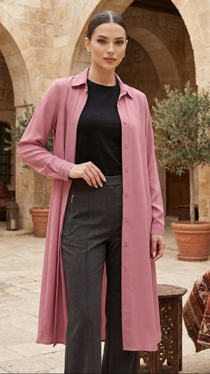 Woman wearing a pink coat in an outdoor setting with arches and plants.
