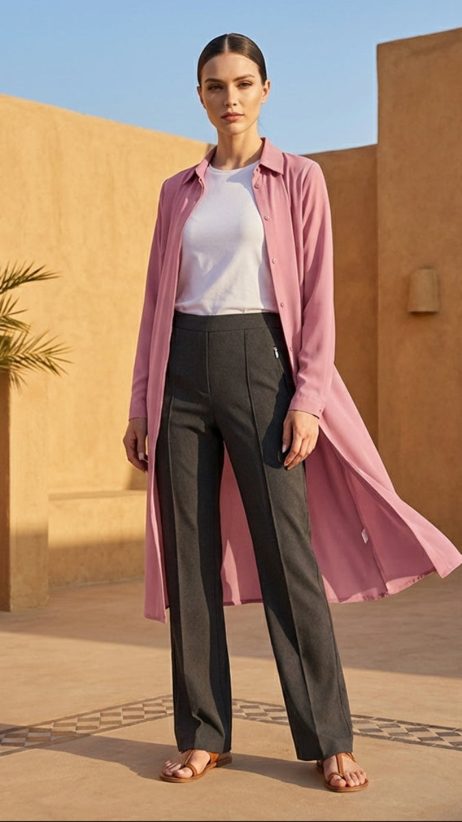 Woman in a pink shirt and black pants standing in a sunlit outdoor setting with architectural elements.