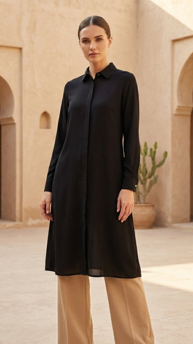 Woman wearing a black dress standing in a courtyard with arches and plants.