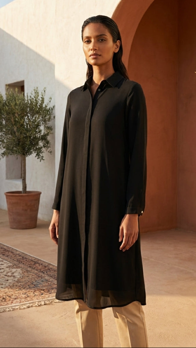 Woman in a black dress standing in a sunlit outdoor setting with architectural elements and plants.