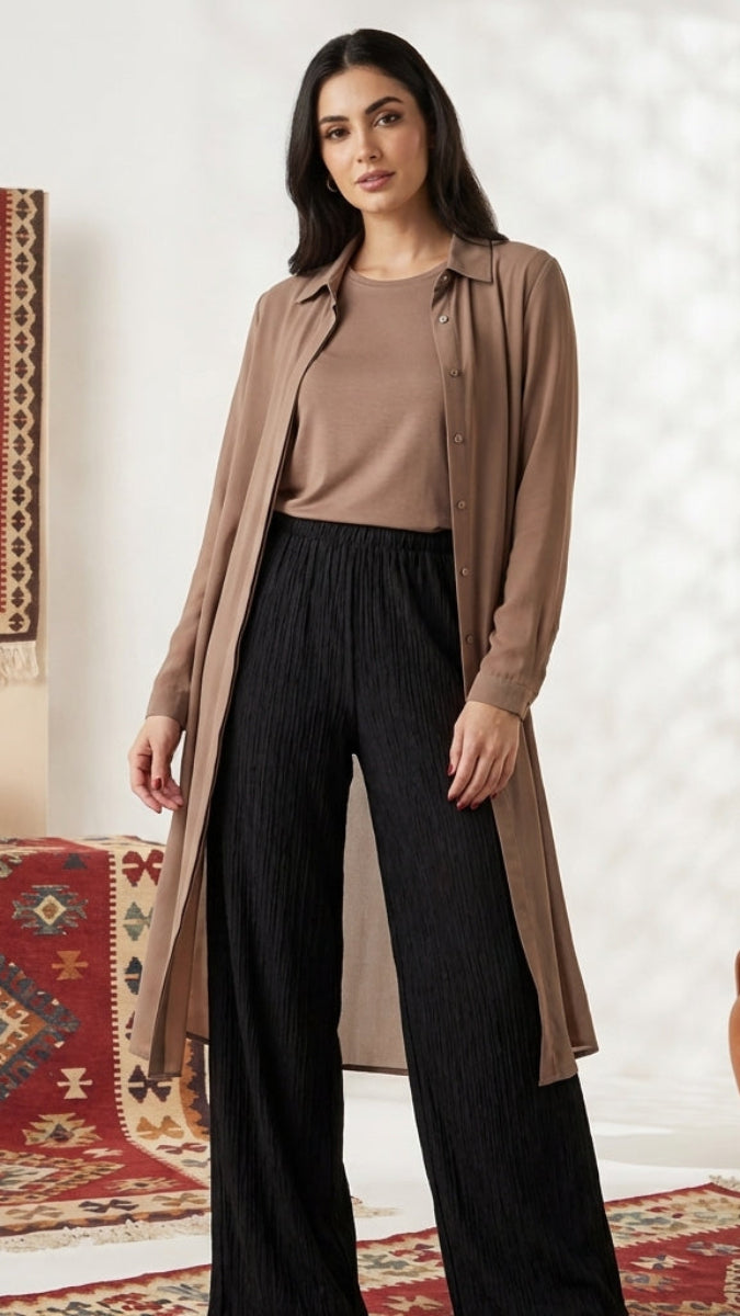 Woman in a brown cardigan and black pants standing in a room with patterned rugs and vases.