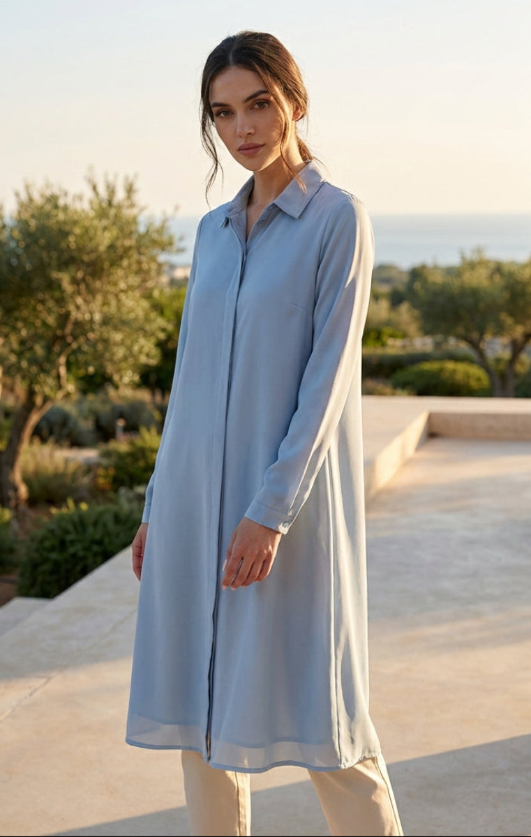 Woman wearing a light blue dress standing outdoors with greenery in the background
