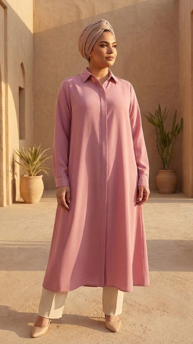 Woman in a pink dress standing in a sunlit outdoor setting with arches and potted plants.
