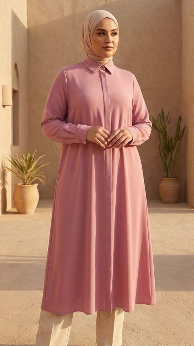 Woman in a pink dress standing in a sunlit courtyard with arches and potted plants.