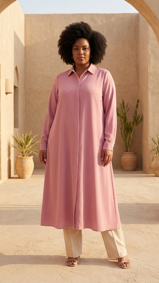 Woman wearing a pink dress standing in a sunlit outdoor setting with arches and plants.