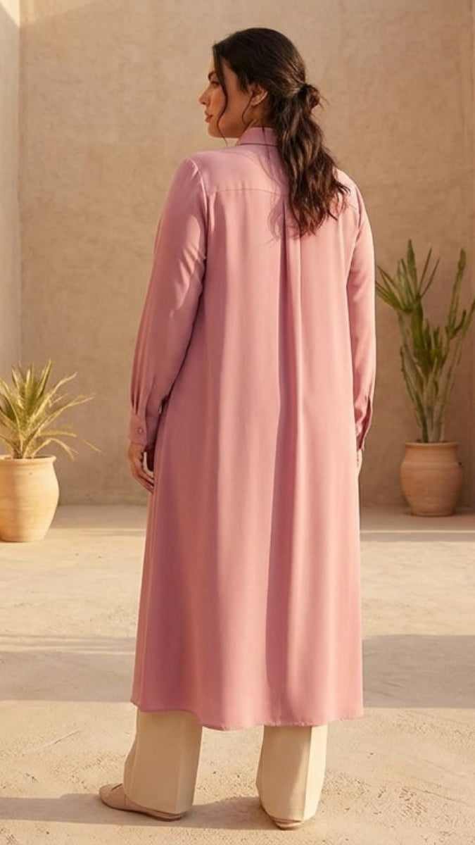 Woman in a pink coat standing in a sunlit, arched architectural setting with plants.