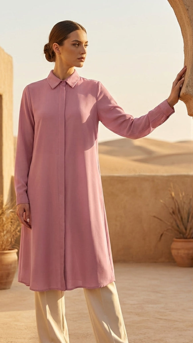 Woman in a pink dress standing in a desert setting with sand dunes and arches.