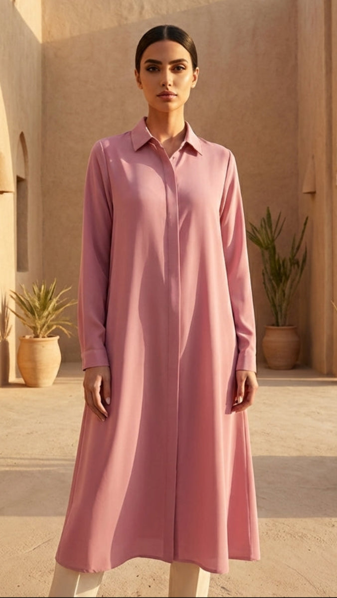 Woman in a pink dress standing in front of a desert building with arches and potted plants.