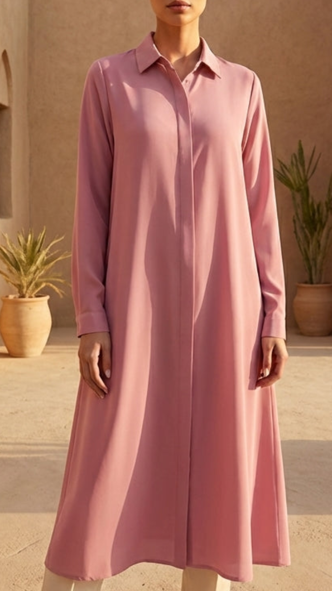 Woman in a pink dress standing in front of a desert building with arches and potted plants.