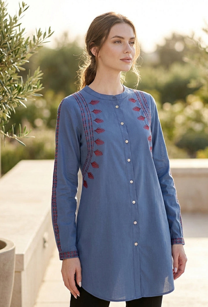 Woman wearing a blue embroidered dress standing outdoors with greenery in the background