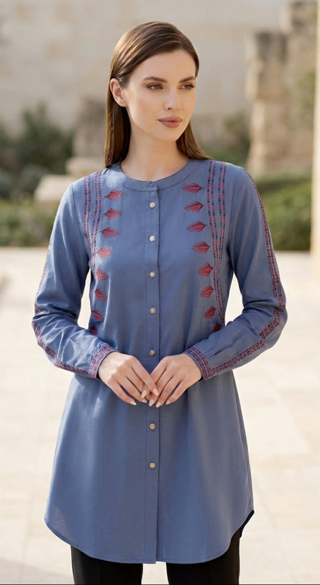 Woman wearing a blue embroidered tunic standing outdoors.