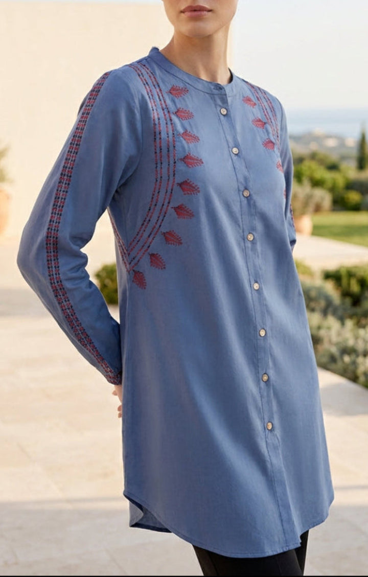 Woman wearing a blue embroidered shirt with a scenic background