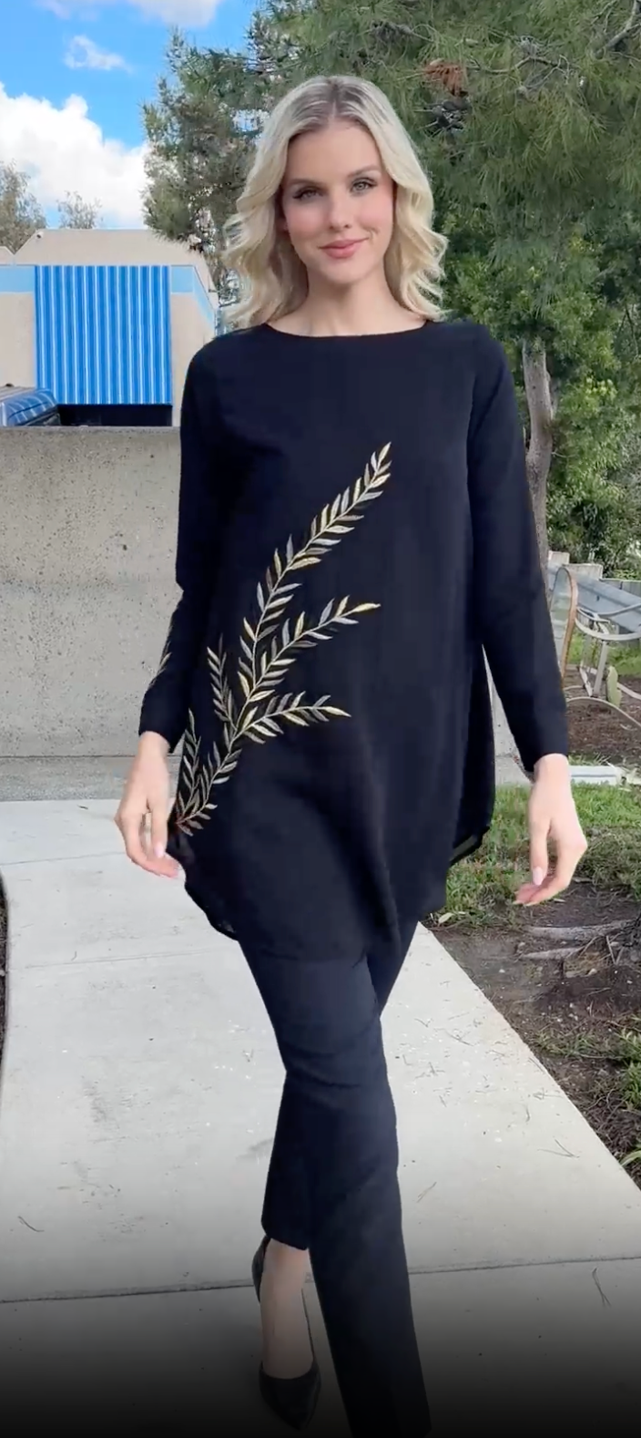 Woman outside walking in Baraka tunic in Black with black pants and heels. 