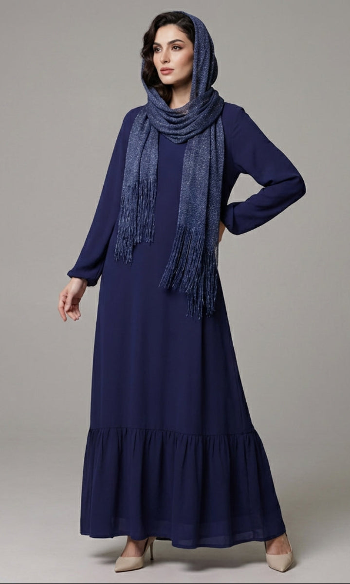 Woman wearing a long navy dress with a matching scarf on a gray background