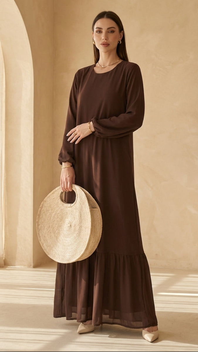 Woman in a brown dress holding a round beige object in a room with neutral decor.