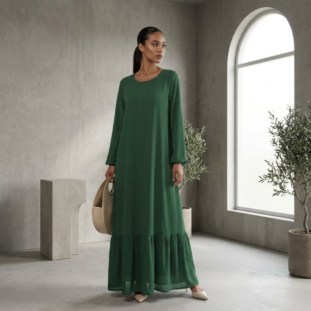 Woman in a green dress standing in a modern room with large windows and plants.