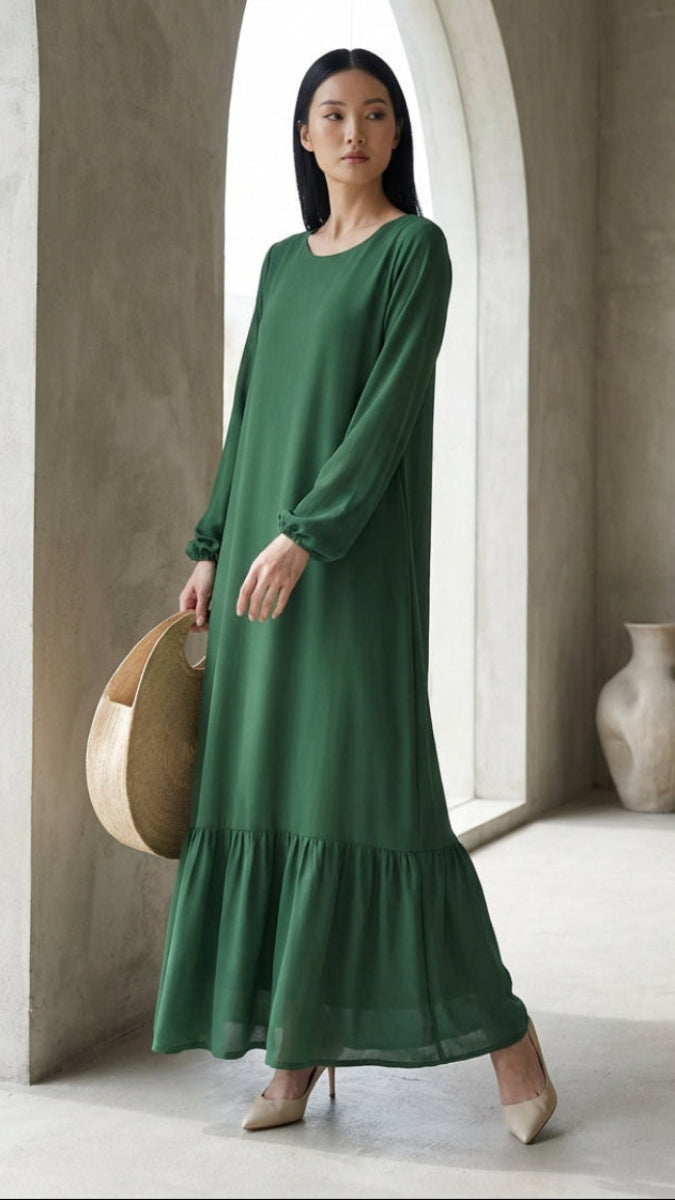 Woman in a green dress standing in a minimalistic room with a vase and basket.