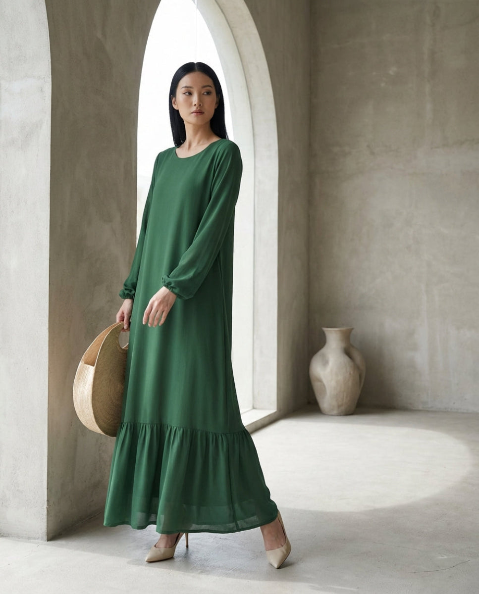 Woman in a green dress standing in a minimalistic room with a vase and basket.