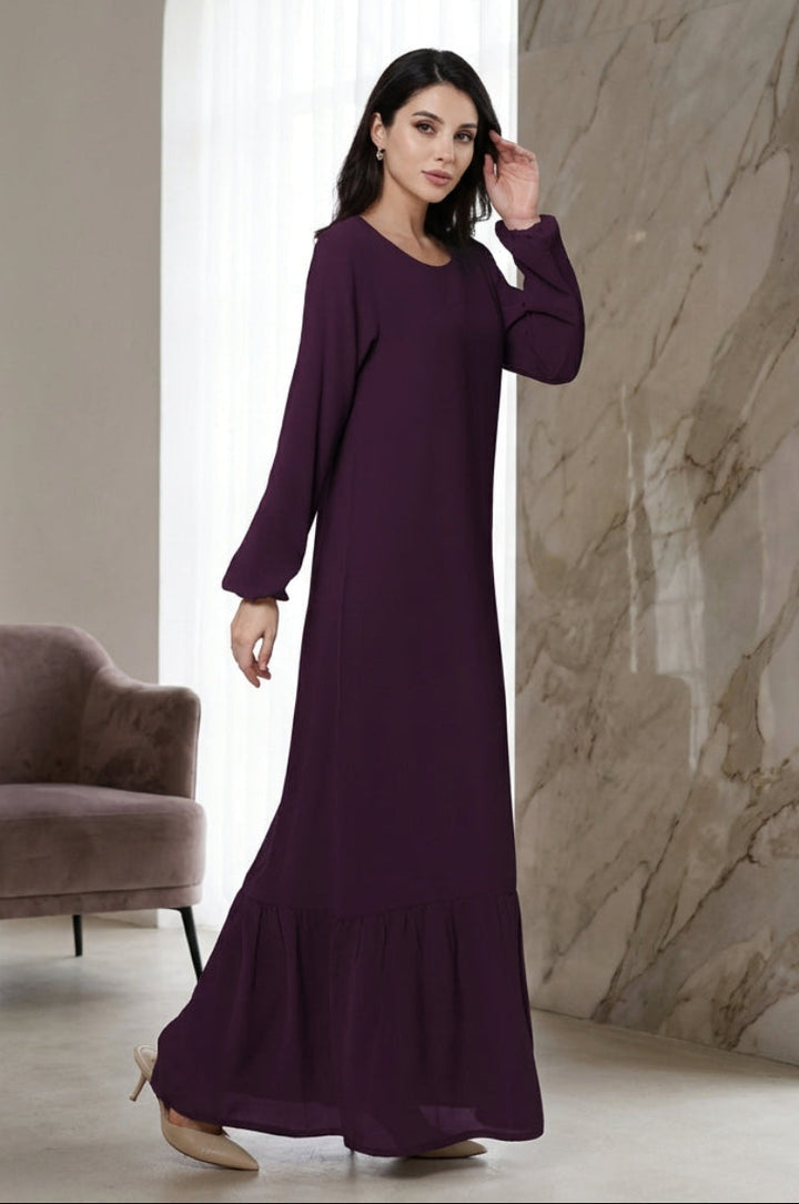 Woman in a long purple dress standing in a modern room with a chair and marble wall.