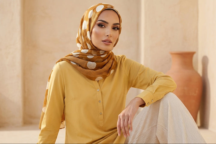 Woman wearing a mustard yellow outfit with a patterned headscarf in a warm-toned interior setting.