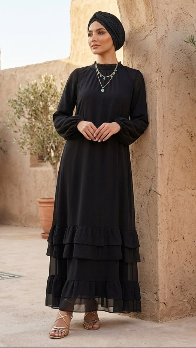Woman in a black dress standing in a sunlit outdoor setting with stone walls and potted plants.