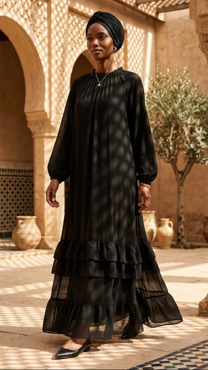 Woman in a black dress standing in a sunlit courtyard with architectural columns and plants.