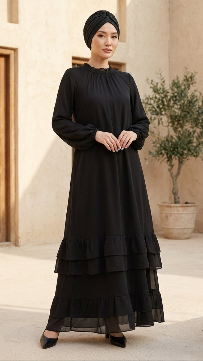 Woman wearing a black dress and headscarf standing in a sunlit courtyard with architectural elements.