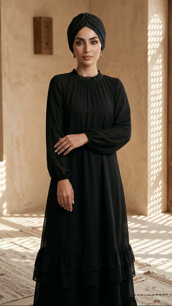 Woman in a black dress and headscarf standing in a sunlit room with architectural elements.