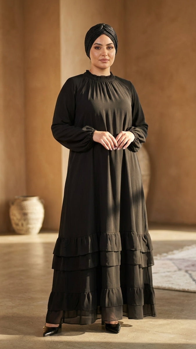 Woman wearing a long black dress with layered skirt in a warm-toned room.