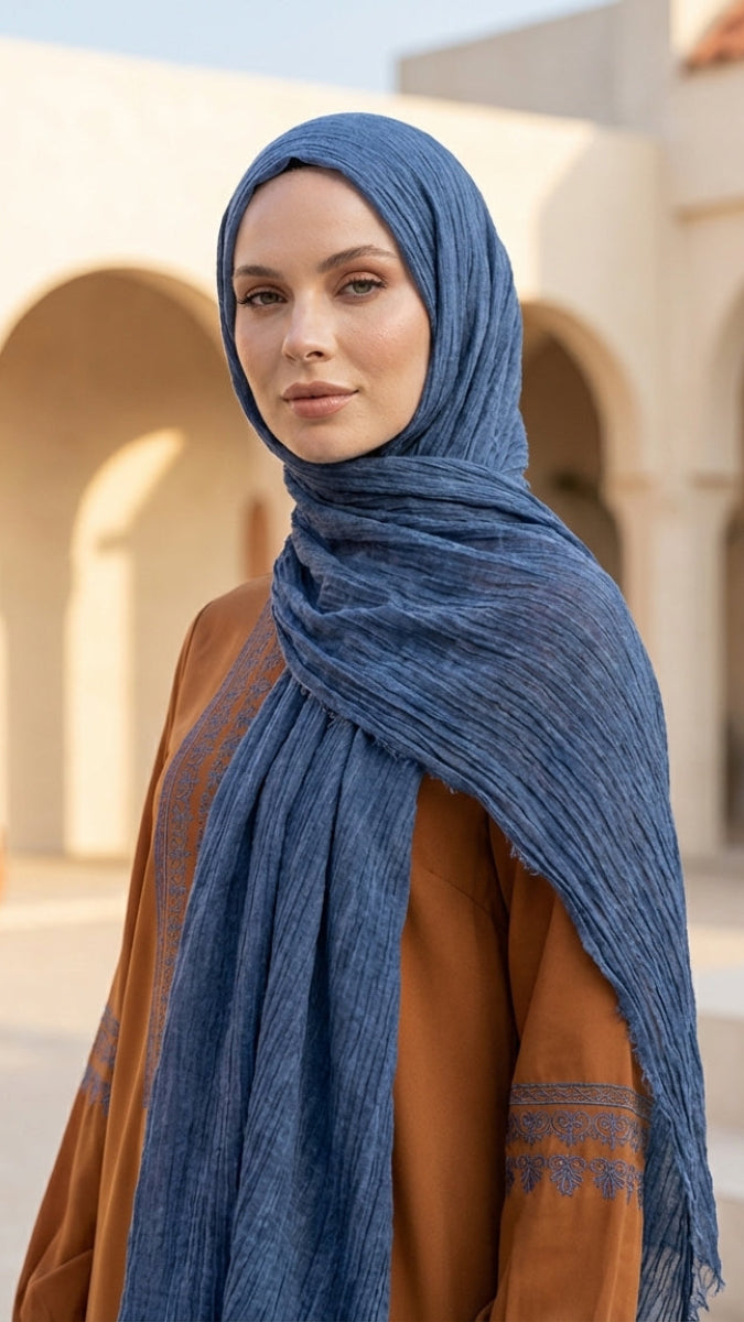 Woman wearing a blue hijab in an outdoor setting with arches and a building.