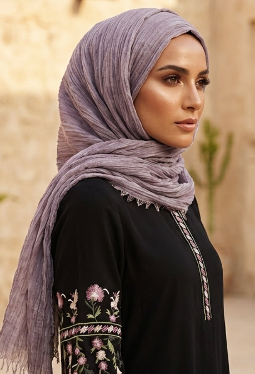 Woman wearing a hijab and black outfit with floral patterns in an outdoor setting.