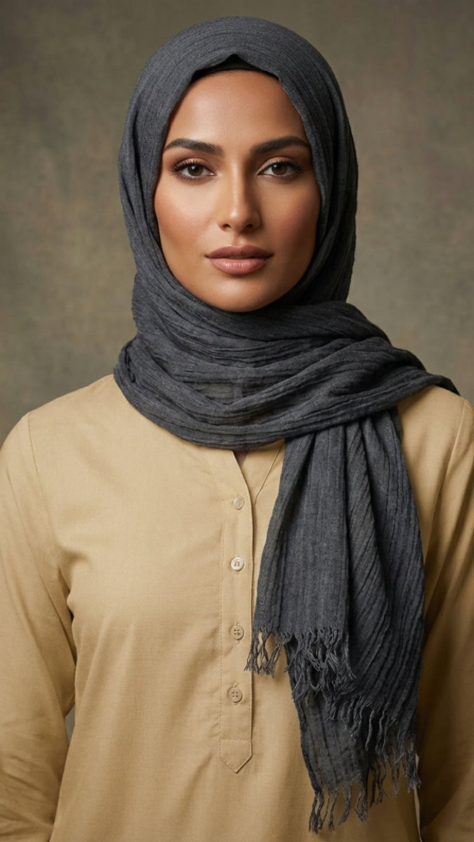 Woman wearing a dark hijab and beige shirt against a brown background