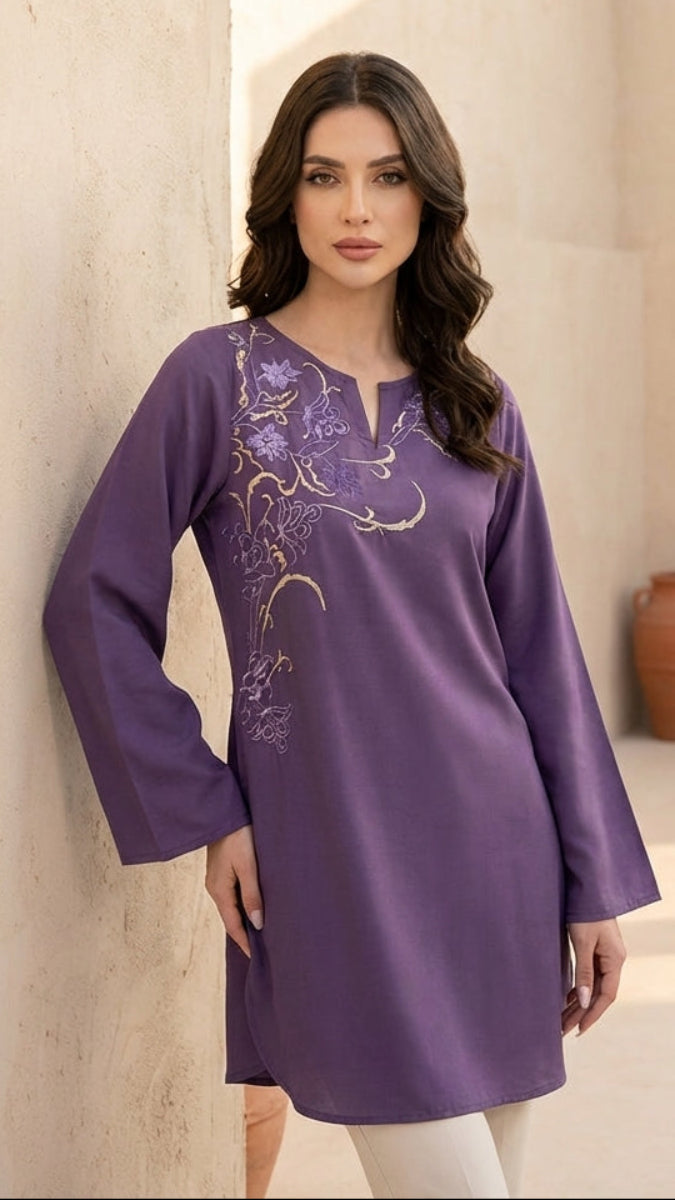 Woman wearing a purple embroidered dress in an outdoor setting with beige walls and terracotta pots.