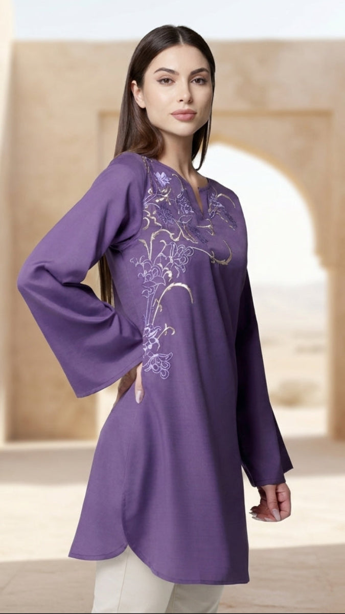 Woman wearing a purple long-sleeve top with floral patterns in an arched architectural setting.