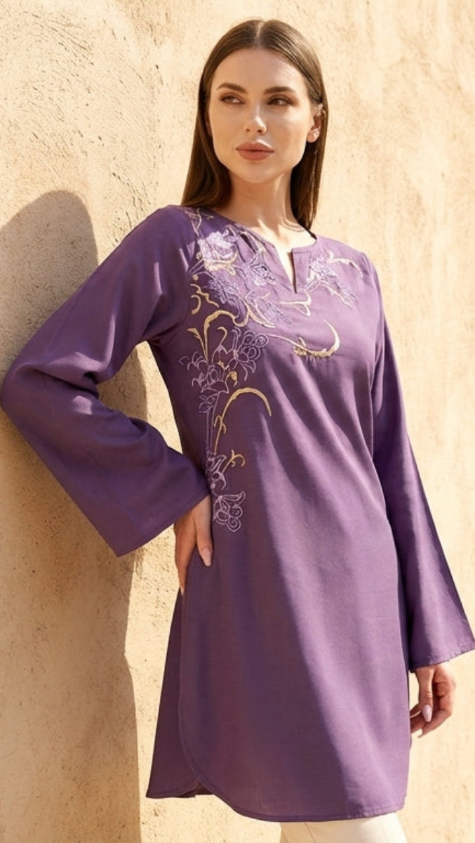 Woman in a purple dress standing against a beige wall with pots in the background