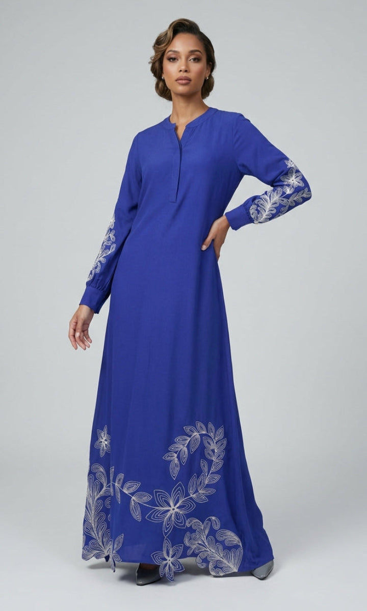 Woman wearing a long blue dress with floral embroidery on a gray background