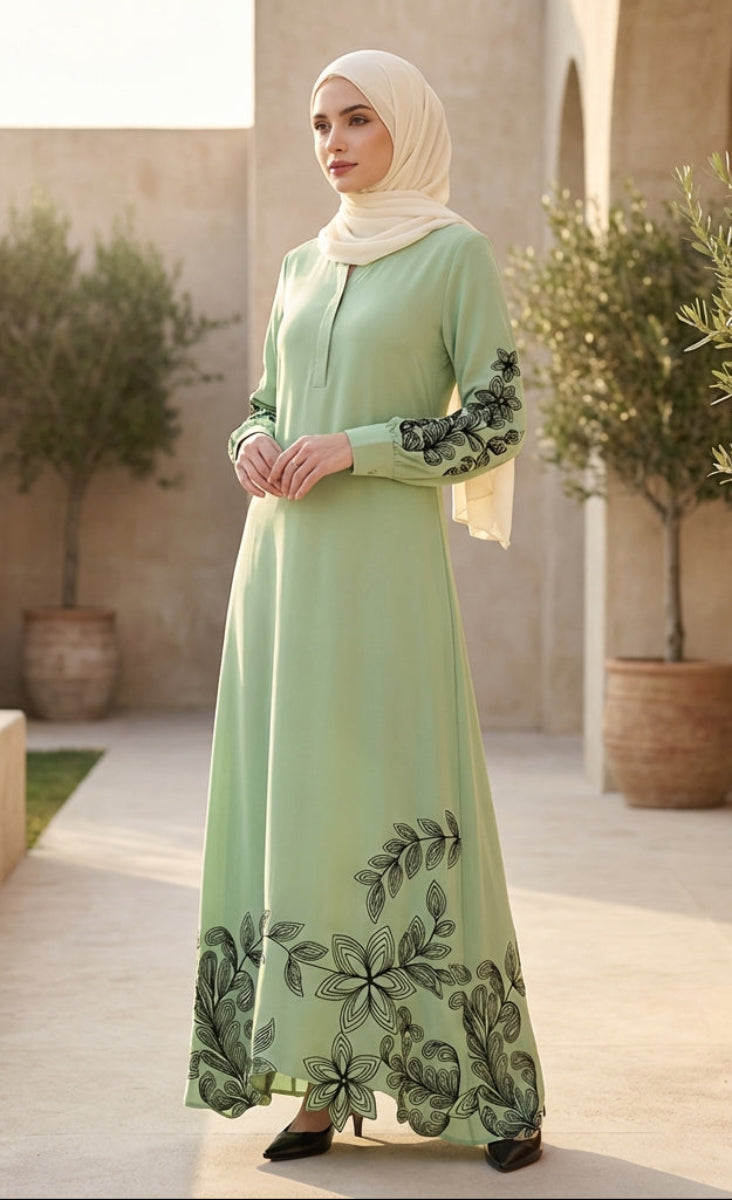 Woman in a green dress with floral patterns standing in an outdoor setting with plants and stone architecture.