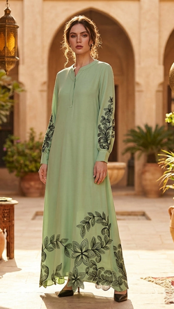Woman in a long green dress with floral embroidery standing in an outdoor setting with lanterns and plants.