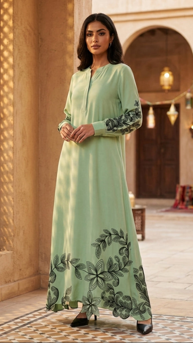 Woman in a long light green dress with floral embroidery standing in an ornate courtyard.