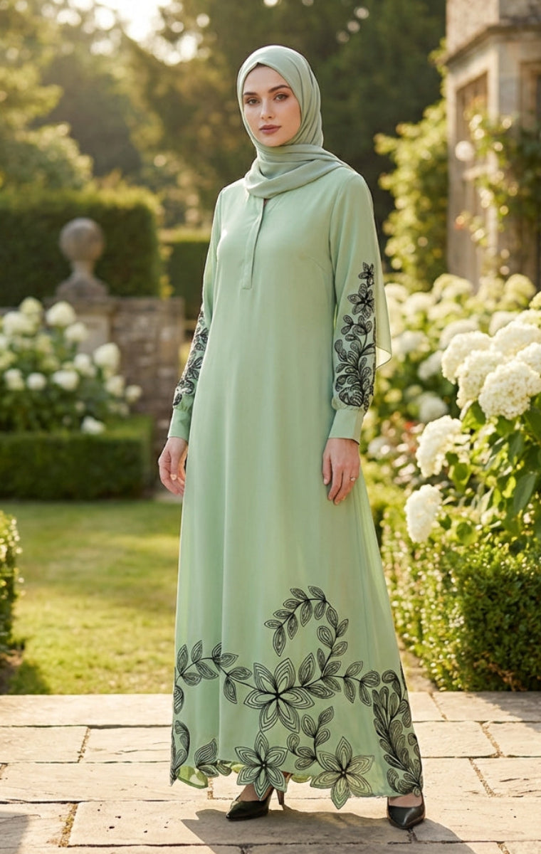 Woman in a light green dress with floral embroidery standing in a garden.